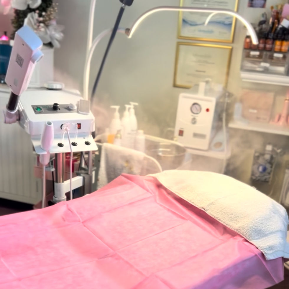 Spa room with a pink-covered treatment bed, steam machine, and skincare products. Soft, relaxing atmosphere with white towels.