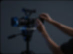 Hände bedienen eine professionelle Filmkamera auf Stativ.