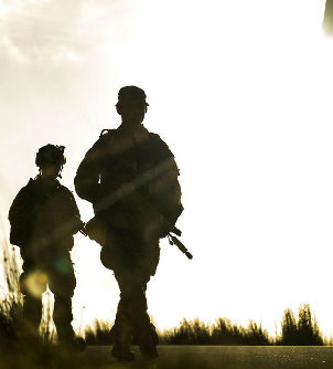 Silhouettes of soldiers walking in a field at sunset, casting long shadows. The bright sun creates a dramatic, intense atmosphere.