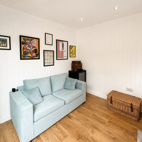Seating area inside a compact garden office in Nottingham with sofa, white grooved walls and laminate flooring.