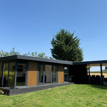 Large L-shaped bespoke garden room in Nottinghamshire. Garden Room is clad in cedar maintenance free slatted cladding and anthracite. Open canopy with dining area and hot tub. 