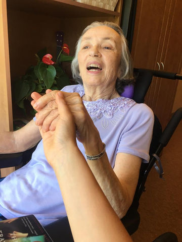 A client smiles as they hold a caregiver's hand