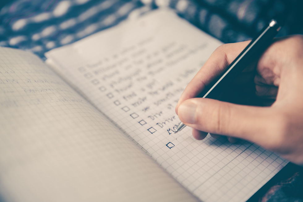 A travel budget checklist in a notebook and a woman's hand adding to it with a black pen.