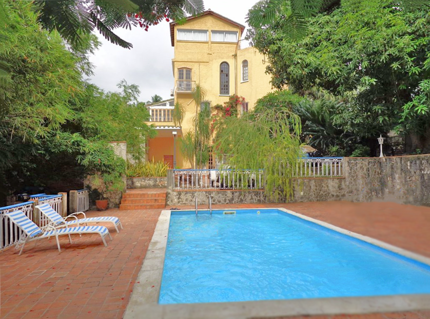 Blue pool and striped lounge chairs on the brick patio at the yellow La Rosa de Ortega Bed and Breakfast in Havana.