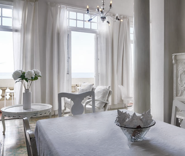 The all white interior of a room in Magical B & B by the Sea Havana that looks out to the sea.
