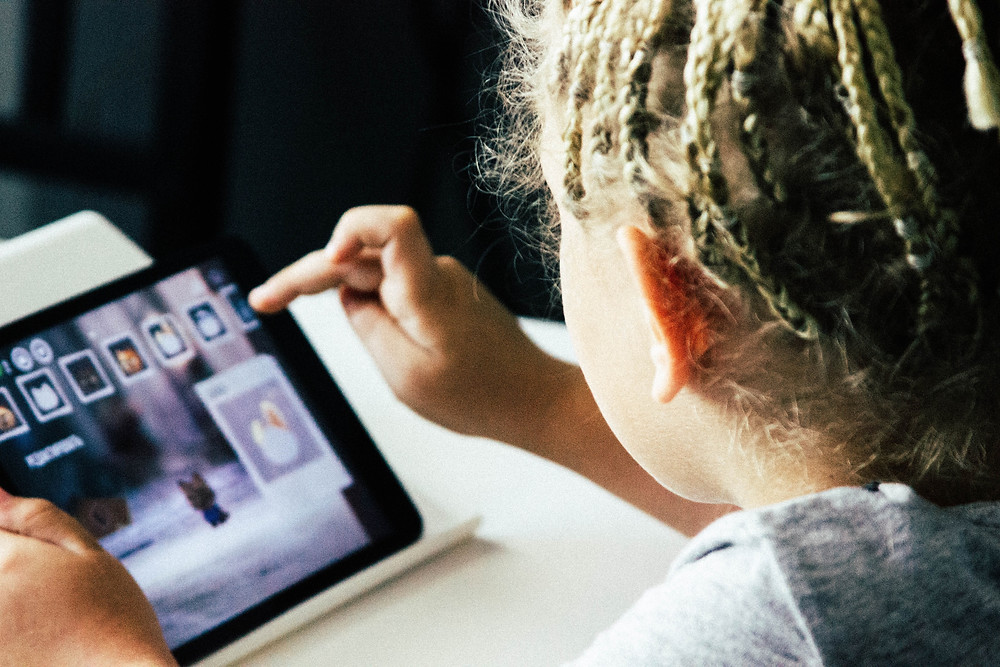 Child with blonde braids and a gray shirt tapping on an iPad during an airplane trip.