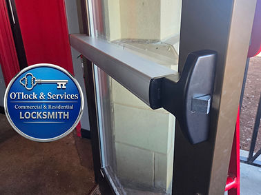Commercial glass door equipped with a panic bar hardware system, featuring the blue circular logo for OTlock & Services Locksmith, which displays a key icon and the text 'Commercial & Residential LOCKSMITH