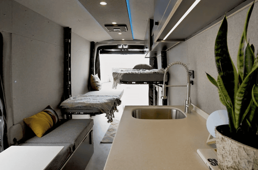 Longhorn camper van interior with Corian kitchen counter, cozy decor, and staggered Code 7 bed platforms, designed by Paradigm Van Conversions for a stylish, comfortable travel experience.