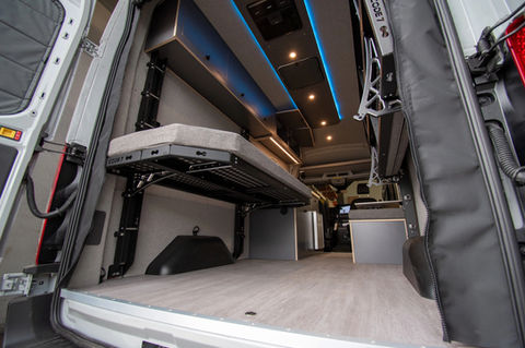 Rear view of Voyager Ford Transit camper van with Code 7 adjustable bed system, full-length cabinets, and blue accent lighting.