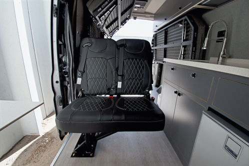 Optional fold-down seat for two in Transit camper van layout, offering extra seating flexibility for friends or family, designed by Paradigm Van Conversions.