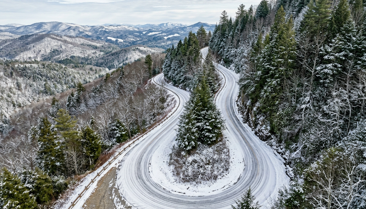 High-angle view of a winding mountain road bordered by trees in winter.