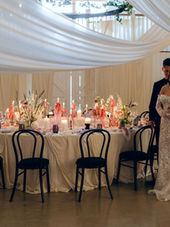 The beautiful White Barn in South Petherton shot by Tara Statton. A Beautiful Bride and Groom stood by a stunning circular table adorned with candles and florals. Black Chairs and drapes. 