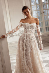 In cappuccino or ivory, this A-line gown is a masterpiece of 3D lace, with a hand-decorated corset and delicate decolletage. The sweetheart neckline, open shoulders, and long sleeves create a romantic and vibrating silhouette, offering a soft yet captivating elegance.