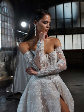SALE DRESS ~ Our Chevelle princess wedding gown represents where Evie Young turns ordinary into extraordinary with reimagined silhouettes and fashion forward style.
Here from our Noir collection, is the Chevelle gown in the classic ballgown shape transformed using modern abstract lace and long sleeves. Her strapless illusion bodice features strong exposed boning construction that creates a sexy, lifting corset for the bust area, as well as an elongated lowered V-shaped waistline that shapes and accentuates the waist.
Off the shoulder illusion fitted long sleeves are very popular in fashion circles and add arm coverage. Her A-line skirt has a full ballgown effect but is light and airy, with a slimming flat front.
The sexy high front leg split reveals that peekaboo skin moment for a youthful touch which grabs attention as the bride walks. The strapless eyeline continues in the back with button detailing and dramatic all-over lace through to her train. Shown in ivory with a nude mocha underlay.
Was £2148
Sale Price £995
