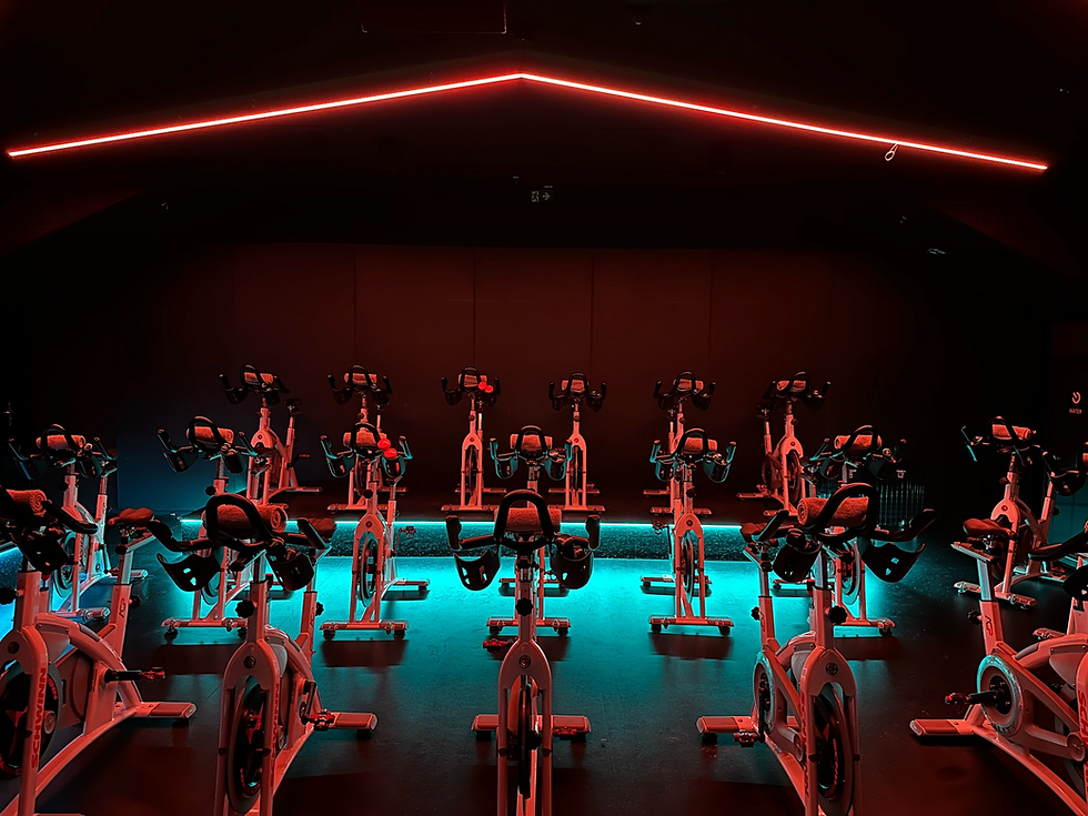 Rows of stationary bikes in a dimly lit gym with red overhead lights. REVOLUTION RIDE. Indoor cycling. Spinning