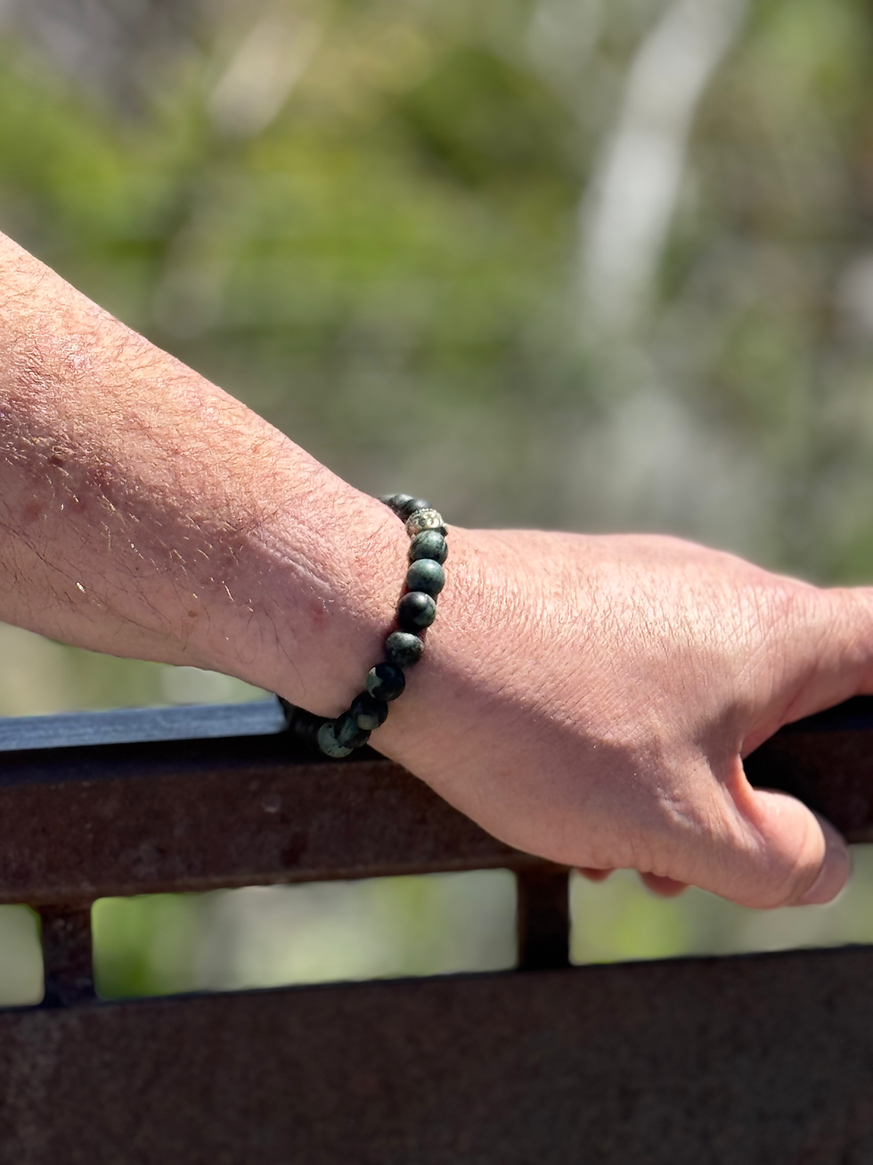 Thumbnail: Man's arm wearing Bontà Verdi Bracelet, resting on a metal railing; outdoors in nature.