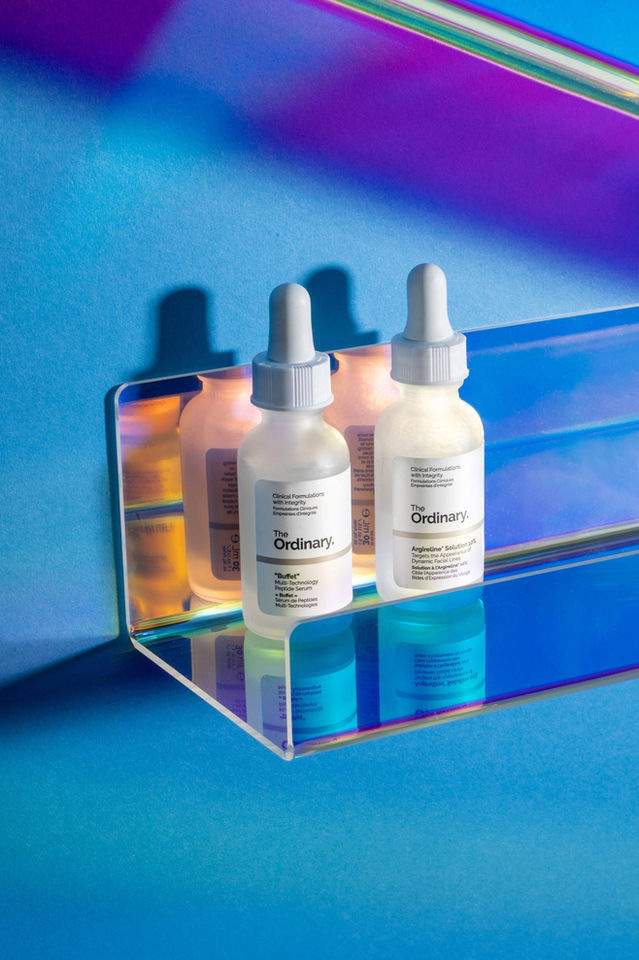 Creative pack shot of 2 small white bottles on reflective plexi glass shelves against a blue wall