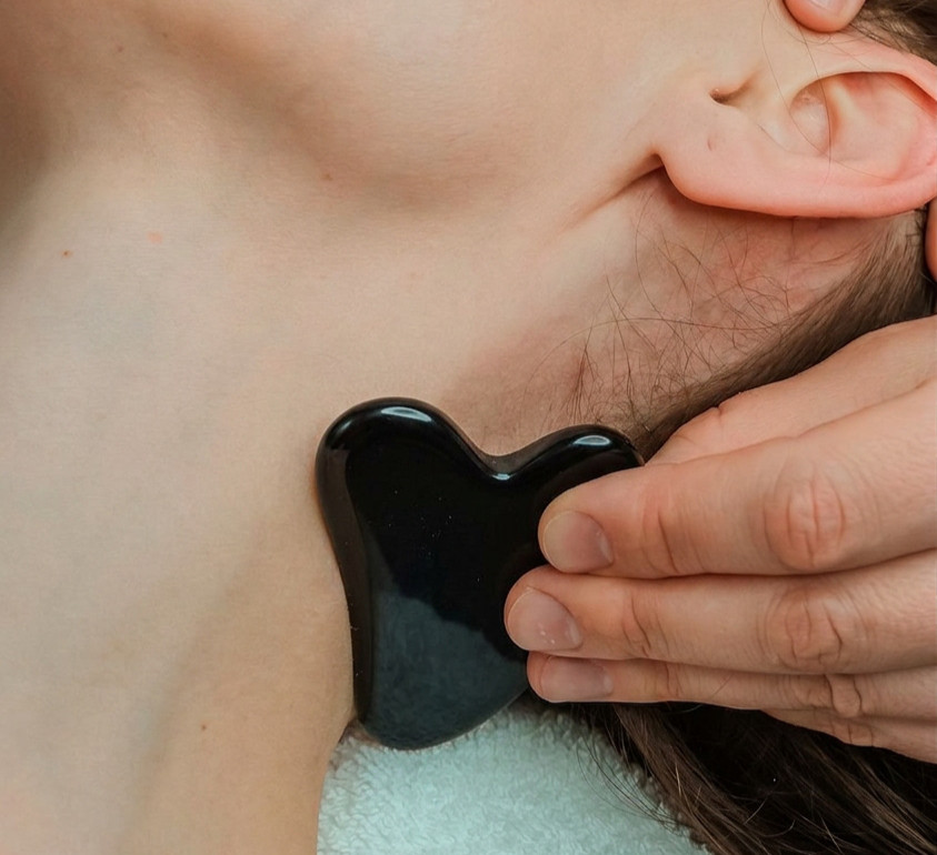 Hand applying black Gua Sha stone to patient's neck