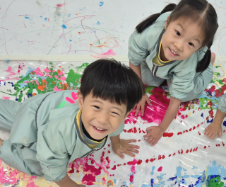 Two children sitting on the floor, smiling and painting with colorful paints.
