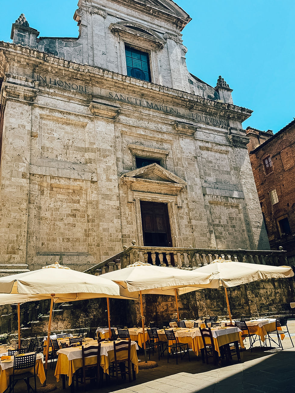 Outdoor café with yellow tablecloths and umbrellas, set against an ornate stone building under a clear blue sky.