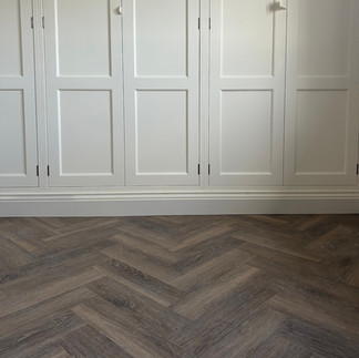 Dark oak herringbone flooring in front of cream fitted wardrobes