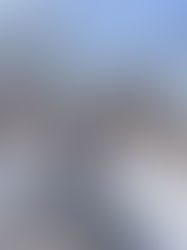 Person in winter attire joyfully posing on a snowy park trail, surrounded by bare trees, under a clear blue sky on a sunny day.