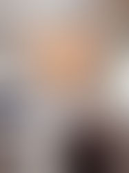 Woman in a cozy robe sipping coffee on a bed in a serene bedroom. Instruments hang on the wall, and warm light illuminates the scene.