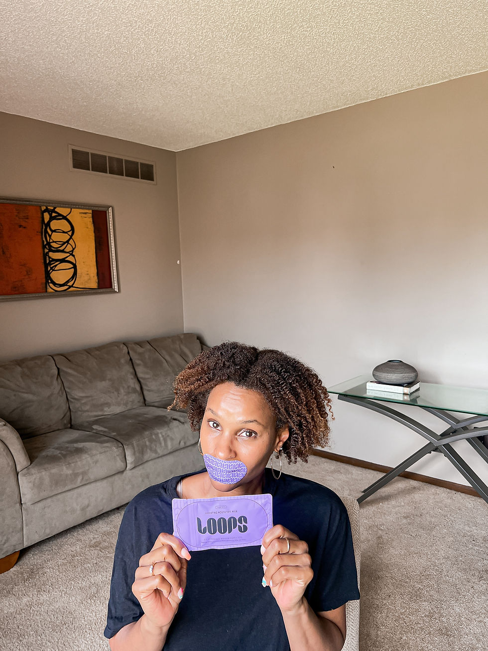 Woman in a living room holds a purple Loops mouth mask package and wears a matching mask, looking at the camera.
