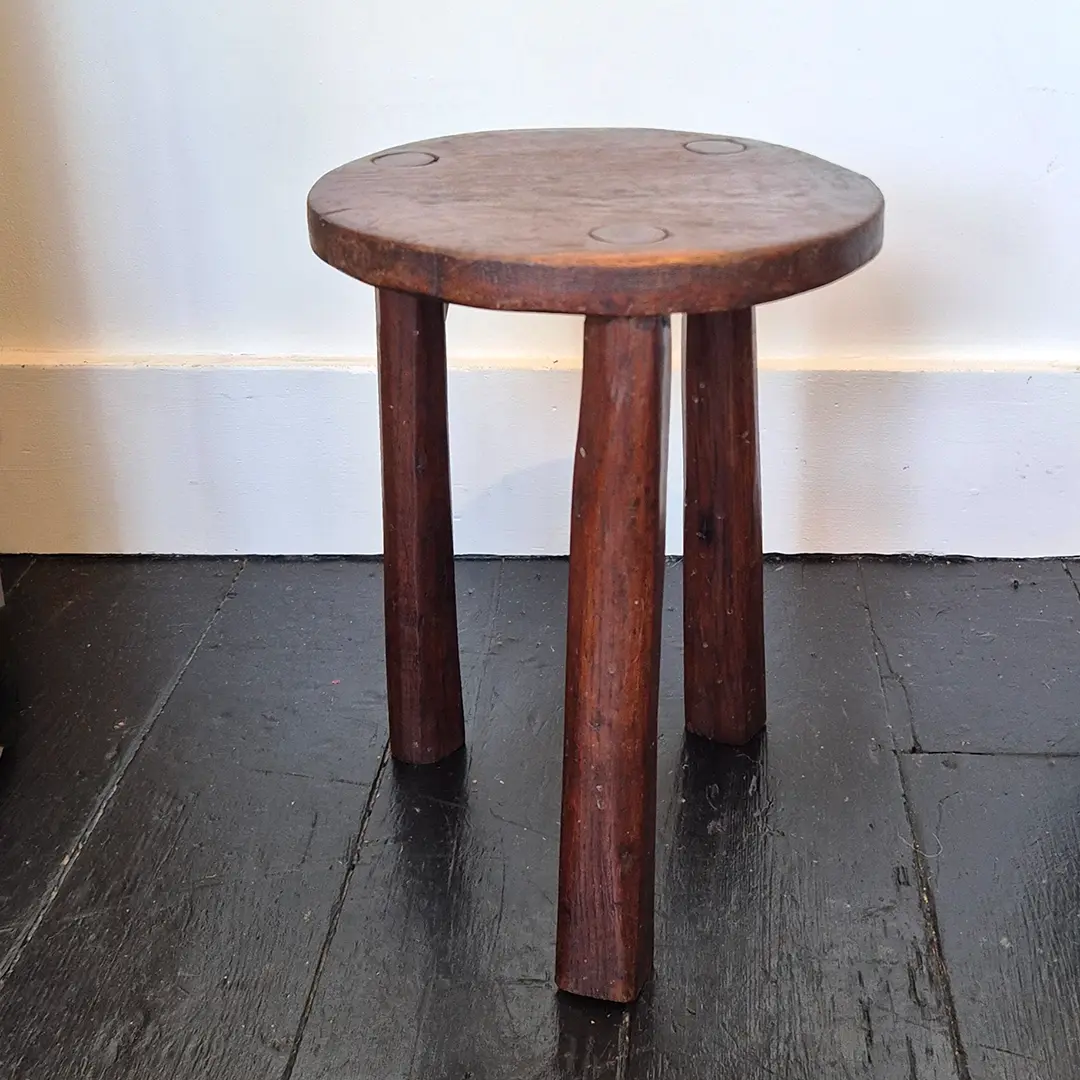 A three legged vintage wooden stool in dark wood with a lovely aged patina - front view