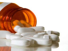 The image shows an orange prescription bottle tipped over, with white pills spilled out onto a reflective surface. The label on the bottle is partially visible, indicating it contains medication. The scene suggests themes of medication use, potential overuse, or the importance of proper dosage in a healthcare context. The background is plain, focusing attention on the bottle and pills.
