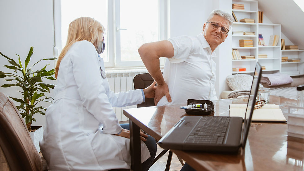 Doctor examines a man with back pain in a bright office. The man looks uncomfortable. A plant, laptop, and books are in the background.
