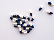 Blue and white capsules scattered on a white background, grouped mostly to the left. Mood is clinical and organized.