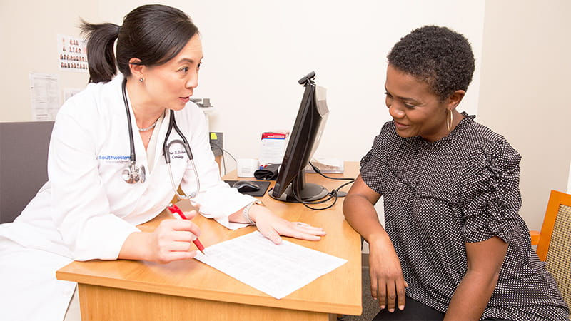 Doctor and patient in a clinic. The doctor in a white coat explains a document, while the patient listens. Desktop computer in the background.