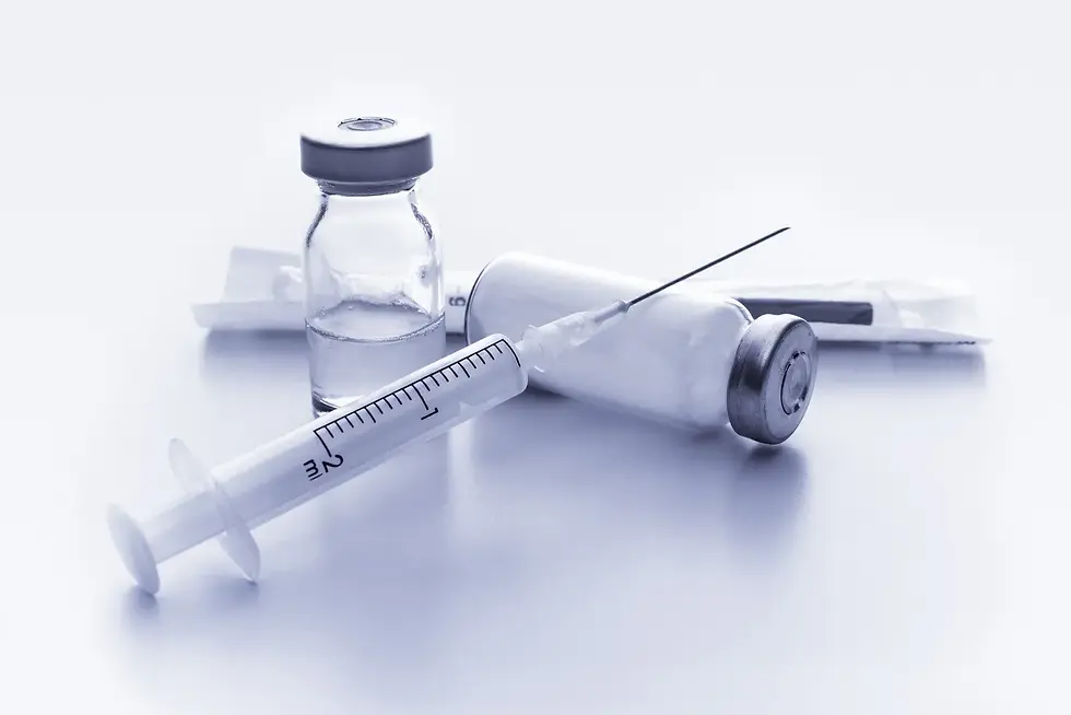 A syringe and two vaccine vials on a white surface. The setting is clinical and sterile, with a cool, blue-toned color scheme.
