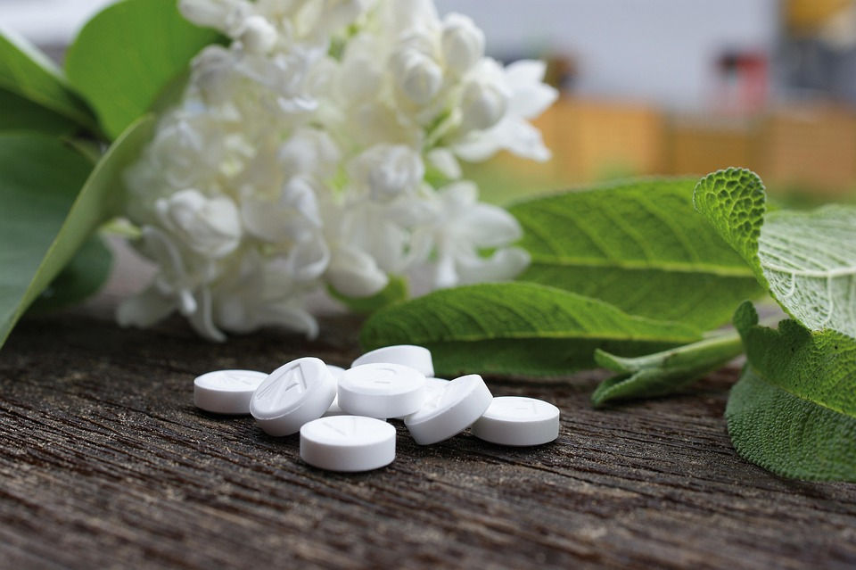 White pills on a wooden surface with green leaves and white flowers in the background. Calm, natural setting.