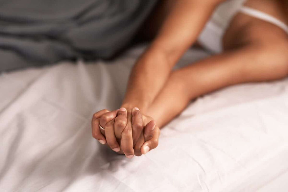 Two people holding hands on a bed, suggesting intimacy. Soft lighting, white sheets, and a calm, cozy atmosphere.