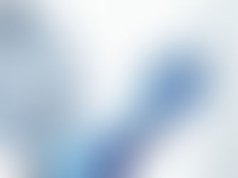 The image shows a close-up of a person wearing a white coat and blue gloves, likely a healthcare professional, preparing a syringe. They are holding a vial in one hand and a syringe in the other, with the needle inserted into the vial to draw a liquid, possibly a vaccine or medication. A stethoscope is visible around their neck, reinforcing the medical context. The background is blurred, focusing attention on the hands and equipment, suggesting a clinical or hospital setting.