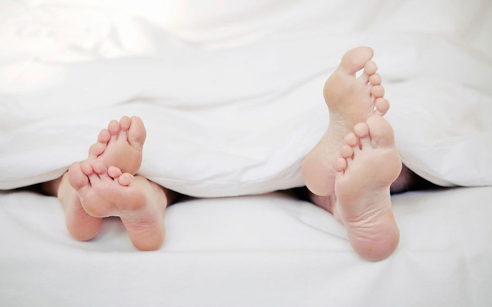 Two pairs of feet peek out from under white sheets. The smaller pair suggests a child, conveying warmth and comfort in a cozy setting.