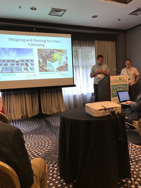 Two speakers presenting about cohousing with a slideshow being projected on a screen.