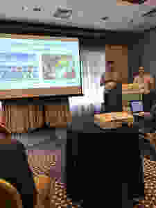 Two speakers presenting about cohousing with a slideshow being projected on a screen.