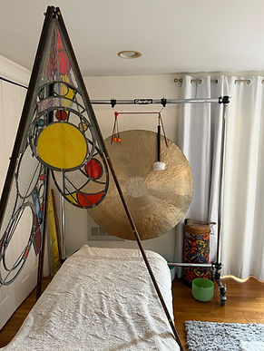 Massage table beneath a stained glass pyramid with a large gong for sound healing, energy work, and retreat experiences.