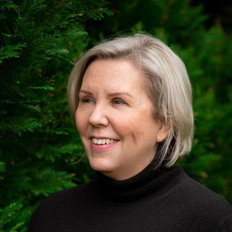 Smiling woman in black turtleneck against green foliage