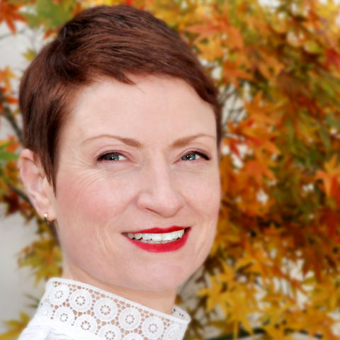 Smiling woman with red hair and white lace top, autumn leaves background