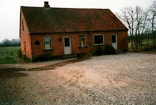 Gammelt længehus i røde mursten med tegltag og gårdsplads med grus