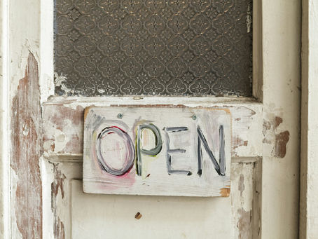 Worn wooden door with textured glass, displaying a handmade "OPEN" sign in colorful, bold letters, creating a vintage feel.