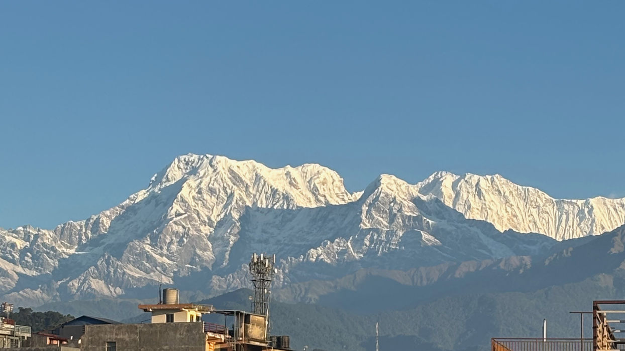 Snow-capped mountains rise above a town under a clear blue sky.