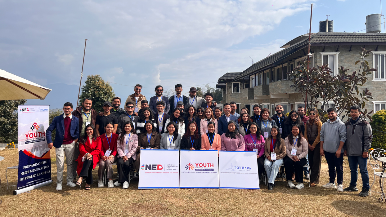 Group photo in front of Youth Initiative Nepal banner outdoors with a building.