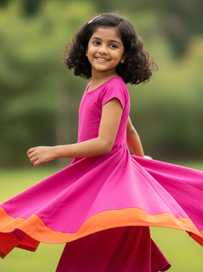 Joyful Indian girl in a vibrant pink and orange twirl dress spinning outdoors.
