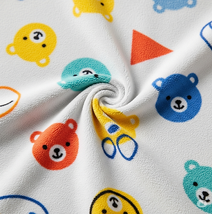 Close-up of soft white pure cotton fabric with cheerful, colorful teddy bear and geometric patterns.