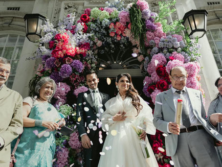 Bride and groom exiting chelsea old town hall through a floral archway as family throw confetti.